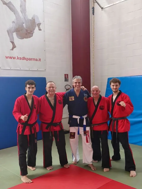 Foto di gruppo sul tatami: allievi in giacca rossa accanto a un maestro in divisa blu