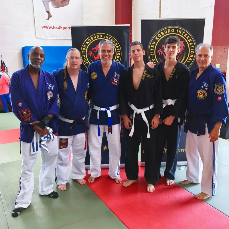 Maestri e allievi in divisa blu e nera, davanti agli stendardi della Ju Jitsu Kobudo International
