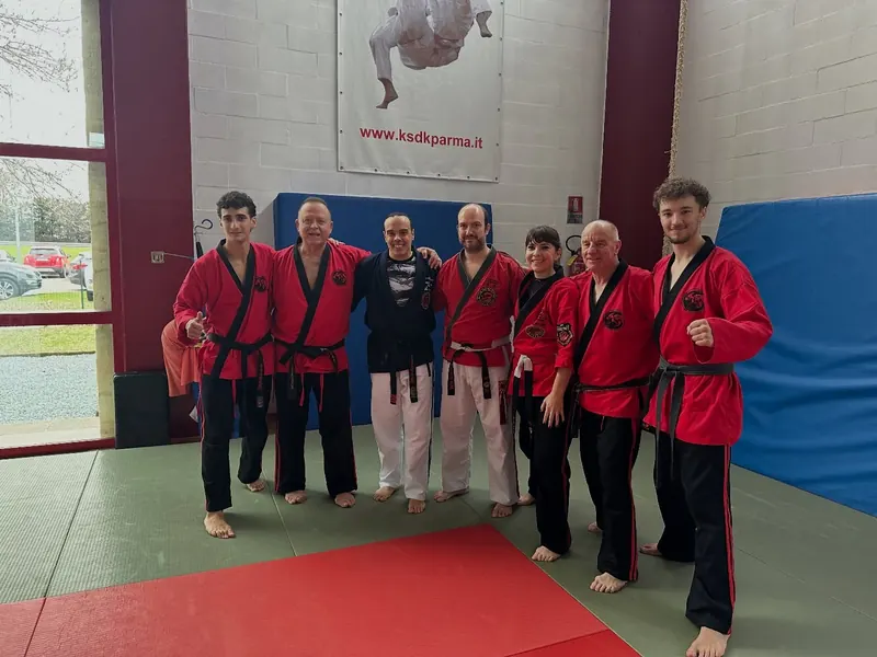 Foto di gruppo sul tatami a fine allenamento, in giacca rossa e cintura nera